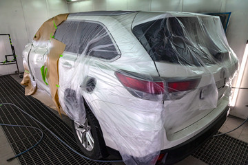Painting the white car SUV in the workshop for body repair. Car covered with paper and envelop from hitting paint.