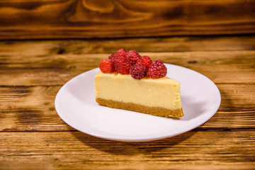 White plate with cheesecake New York and raspberries on wooden table