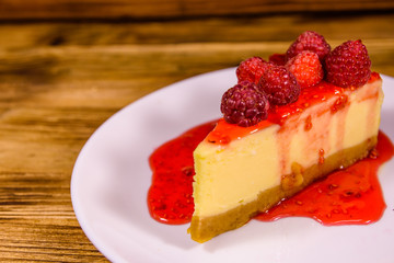 White plate with cheesecake New York and raspberries on wooden table