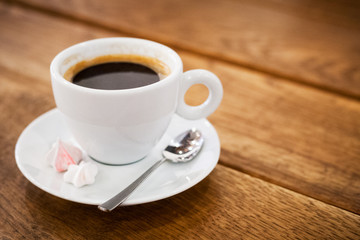 a cup of coffee bize on a saucer and a spoon stands on a wooden table. aromatic hot fresh coffee. wooden vintage table background with diagonal lines. for design and decor. selective focus