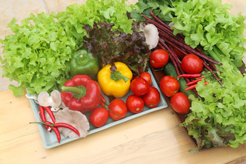 Closeup of organic fresh vegetables in ceramic and wooden plates on wooden table. Preparation for healthy food cooking. 