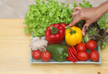 Closeup of woman's hand catching organic fresh vegetables in ceramic plate on wooden table. Preparation for healthy food cooking. 