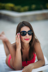Beautiful lady in sunglasses lies on a longer in front of the pool