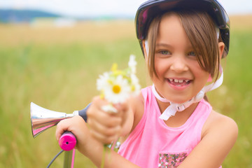 Portrait of a little smiling girl in a protective helmet controls her bike and gives a bouquet of daisies.