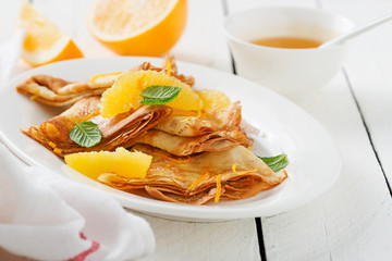 Crepes suzette - pancakes with orange sauce on white wooden table.
