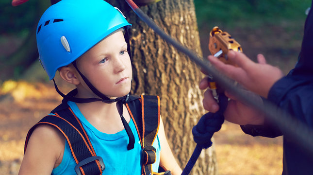 Cute little boy in blue shirt and helmet having fun at the adventure park, holding ropes and prepering to climb wooden stairs. Hobby, active lifestyle concept.