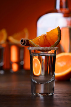 Glasses of tequila with orange and cinnamon sticks on a wooden table.