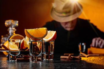 Glasses of tequila with orange and cinnamon sticks on a table in bar.