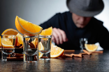 Glasses of tequila with orange and cinnamon sticks on a table in bar.