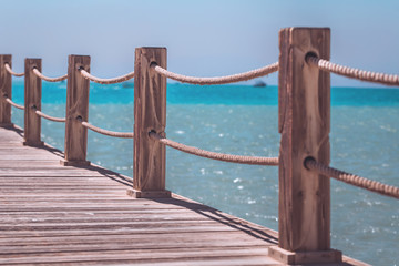 Seaside wooden pier with posts and ropes and sparkling water with copy space