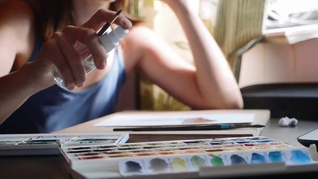 A young woman moisturizes the paint before painting with watercolor, slow motion
