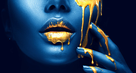 Golden paint smudges drips from the face lips and hand, golden liquid drops on beautiful model girl's mouth, creative abstract makeup. Beauty woman face