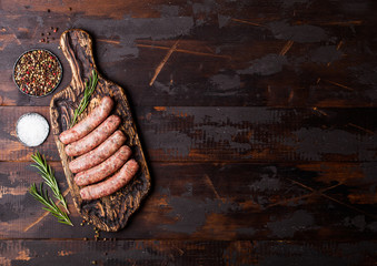 Raw beef and pork sausage on vintage chopping board with salt and pepper on dark wooden background.