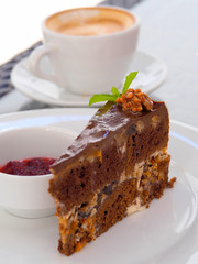 Chocolate Cake on a white plate with a walnut and a cup of coffee in the background