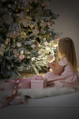 Girl with blond hair in pink dress near the elegant new year tree. Merry Christmas time