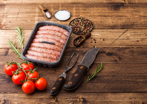 Raw beef and pork sausage in plastic tray with vintage knife and fork on wooden background.Salt and pepper with tomatoes and rosemary.