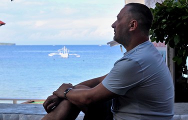 A man looks thoughtfully into the sea at the boats