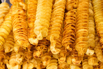 Spiral potatoes fried, on wooden sticks, spiral. Selling food at the market. Unhealthy fried food. Street food, a spiral fried potato on a stick