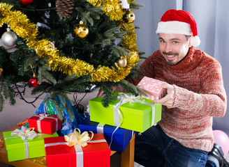 man wearing Santa puts gifts under the Christmas tree