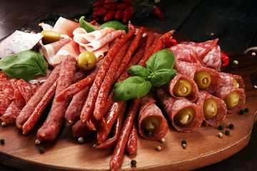 Food tray with delicious salami, pieces of sliced prosciutto crudo, sausage and basil. Meat platter with selection