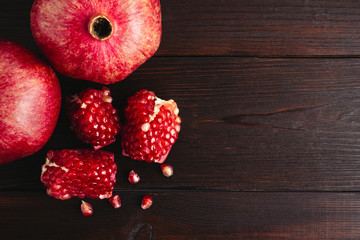 Pomegranate seeds and whole fruits on the dark brown wooden planks, top view
