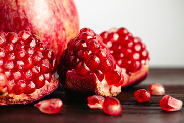 Pomegranate seeds and whole fruits on the dark brown wooden planks and white background, close-up view
