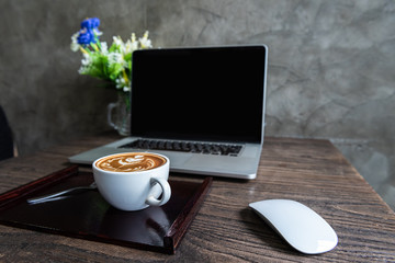 Latte art coffee with blank screen of laptop computer on wooden table
