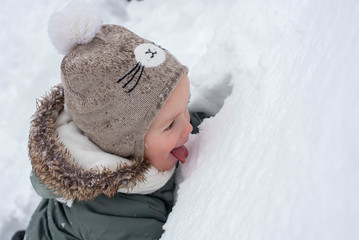 Adorable little boy in warm clothes eating snow and having fun outdoor