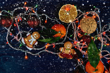 Obraz na płótnie Canvas Lovely Christmas decoration close-up. New Year's things and sweets on a black wooden table. The gingerbread man keeps a cola of chewing marmalade.