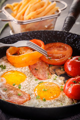 Fried eggs with bacon and tomatoes in an old cast-iron pan. Close-up