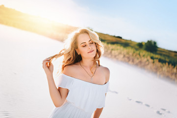 Blond girl enjoying a walk on the white sand at sunset. Portrait of a beautiful woman in the desert. Love story.