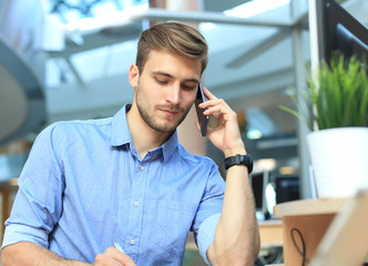 Smiling businessman sitting and using mobile phone in office.