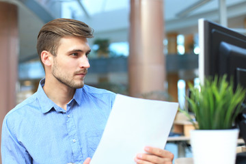 Young businessman reading paperwork at desk in office.