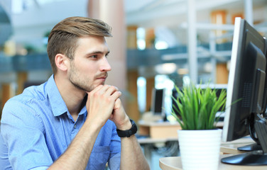 Young man sitting and looking at computer monitor while working in office.