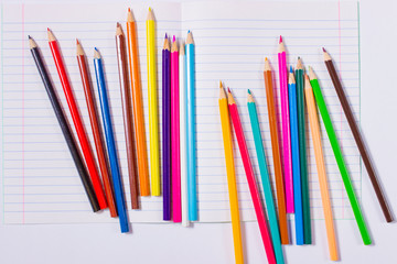 Цветные карандаши на белом листе тетради. - obrazy, fototapety, plakaty