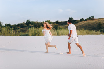 A bearded man and a blond woman run and fool around in the white sand. Love in the desert newlyweds. The love story of fun and love people.