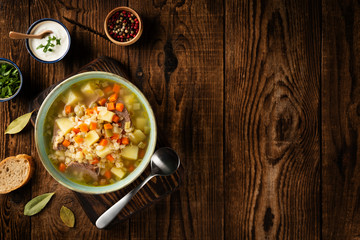 Rassolnik - Traditional Russian soup with pickled cucmbers, pearl barley, meat, pickles, carrots and potatoes on a dark wooden background. Top view