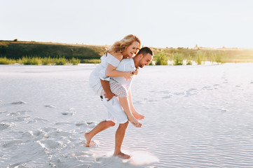 A bearded man and a blond woman run and fool around in the white sand. Love in the desert newlyweds. The love story of fun and love people.