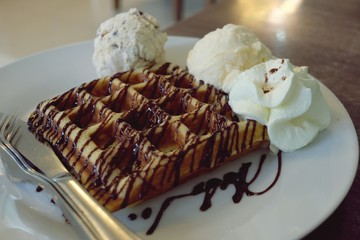 Waffle and vanilla ice cream in white plate on wooden table, copy space
