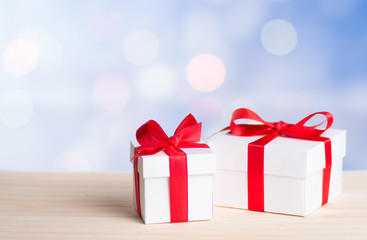 Decorative white gift box with a large red bow standing in fresh snow against a background bokeh of twinkling party lights