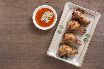 top view of grilled chicken drumette in a ceramic plate served with spicy sauce on wooden table. homemade style food concept.