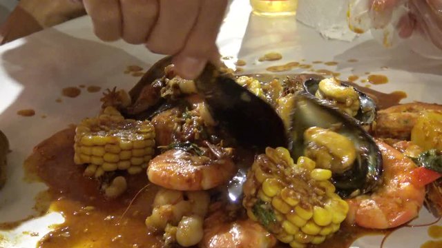 Seafood bucket boil in new orleans spice sauce eating with hand 4k