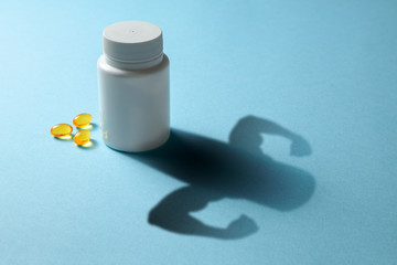 The concept of fish oil gives strength. Bottle with pills and shadow in the shape of the arms with...