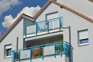 Moderner Balkon mit blau gestrichenem Metall-Geländer und Markise an Neubau-Hausfront
