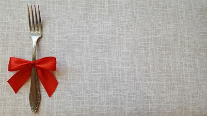 A fork with a red bow lies on the tablecloth. A place to record. Photo for the menu of cafe, restaurant, dining room, pizzeria. A place for a festive menu.