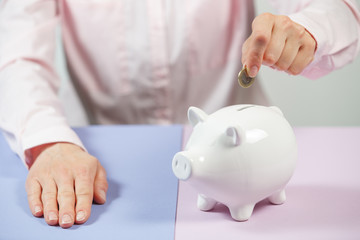 Hand putting coin into piggy bank closeup. Selective focus.