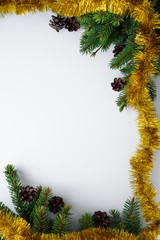 Winter holidays vertical composition made from evergreen conifer branches, cones and gold tinsel. White background with copy space for christmas wishes.