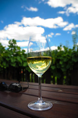 ein glas Weißwein am Heurigentisch vor einem Weingarten unter schönem wolkigen Himmel a glass of white wine on a background of wineyard and beautiful clouded sky, called heaven in a glass of wine