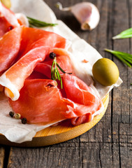 Closeup of thin slices of prosciutto with mixed olives and paprika on wooden cutting board