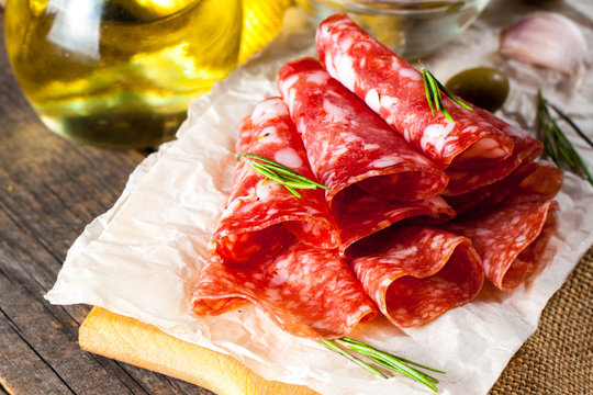 Italian salami with olives and spices on wooden background